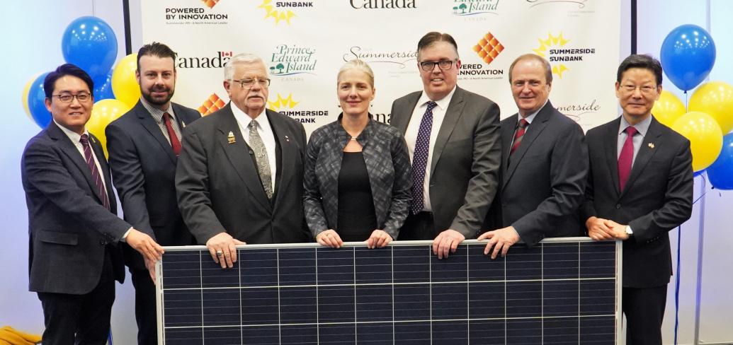 People standing shoulder to shoulder behind a solar panel.