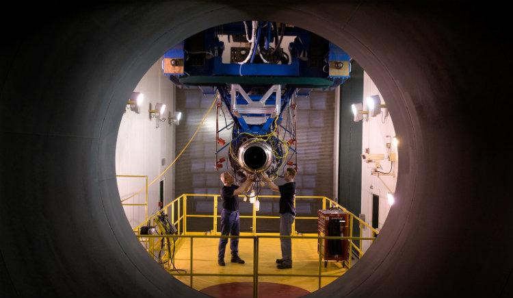 Two man standing and working in a workshop setting on an airplane part